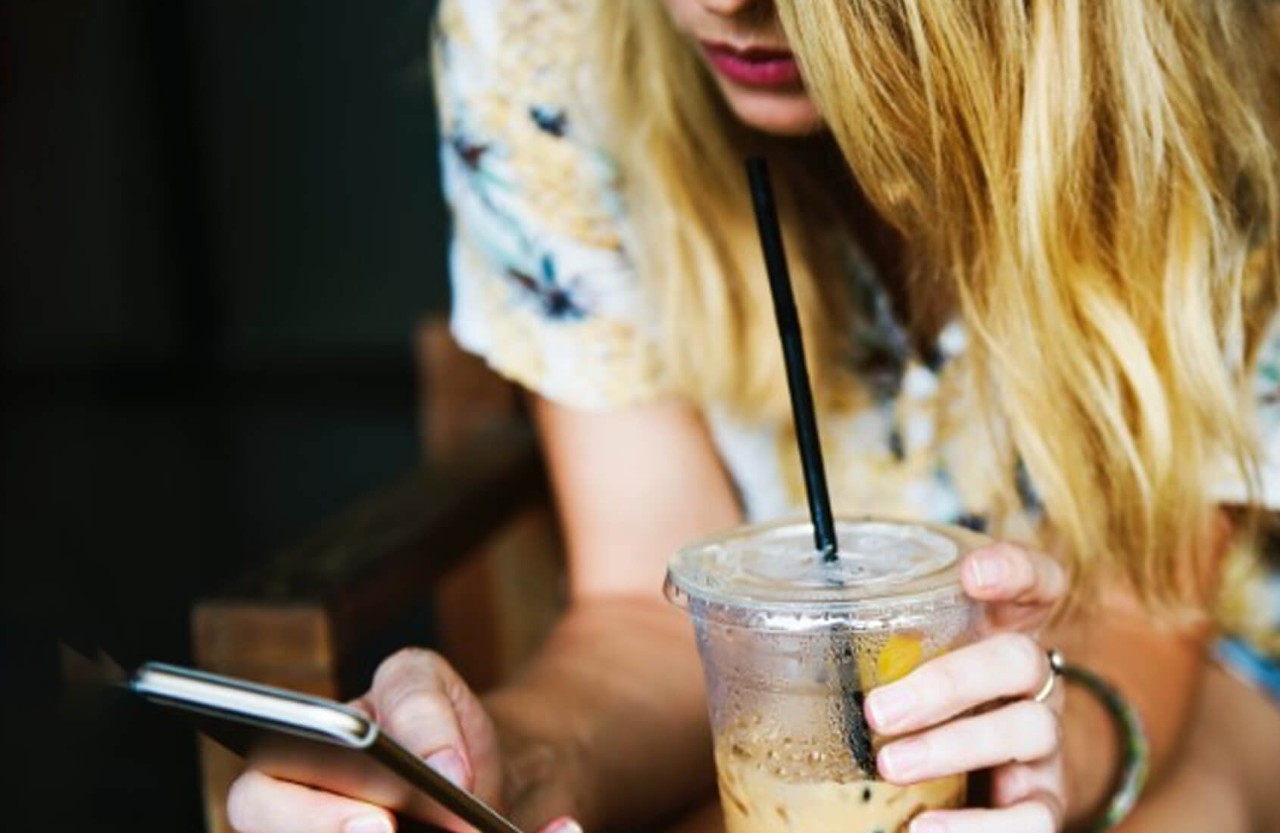 A young woman using phone with an iced coffee
