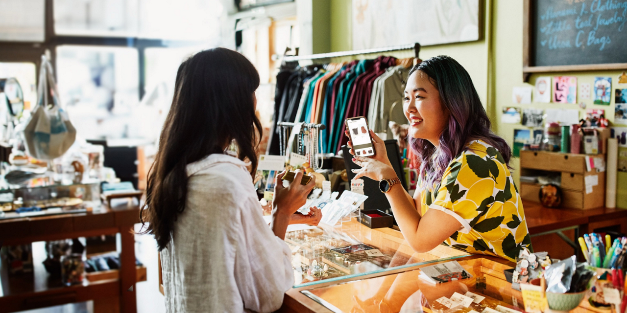 Small business shop owner showing a customer their available stock online using their new mobile handset from Three Business