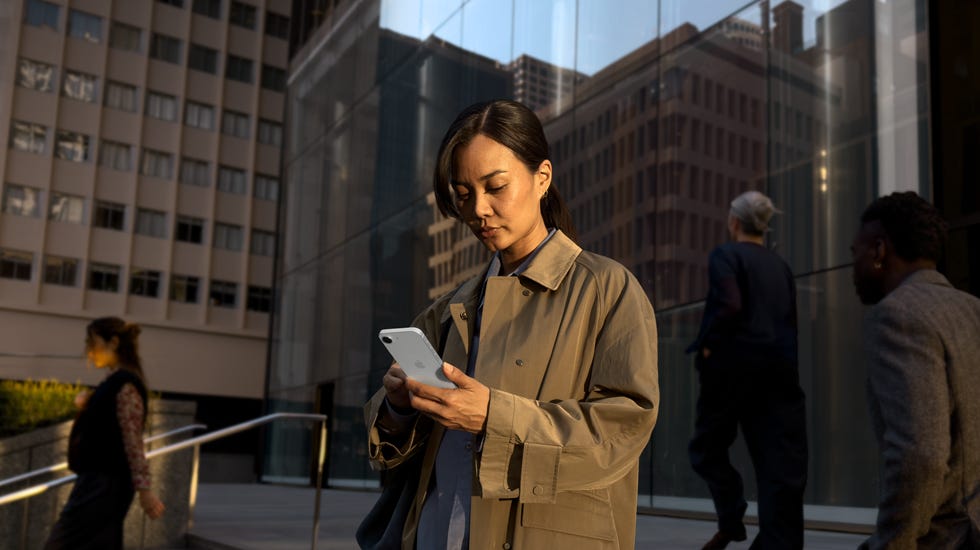 A person using a white iPhone 17e to continue work outside an office building