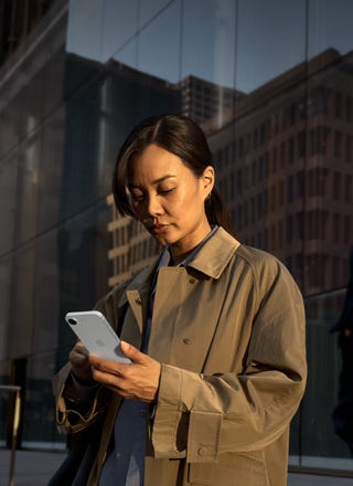 A person using a white iPhone 17e to continue work outside an office building