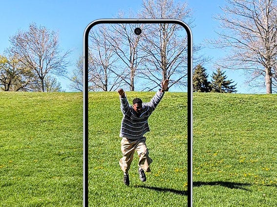 A man joyfully jumps in a grassy park, viewed through the frame of a Pixel phone