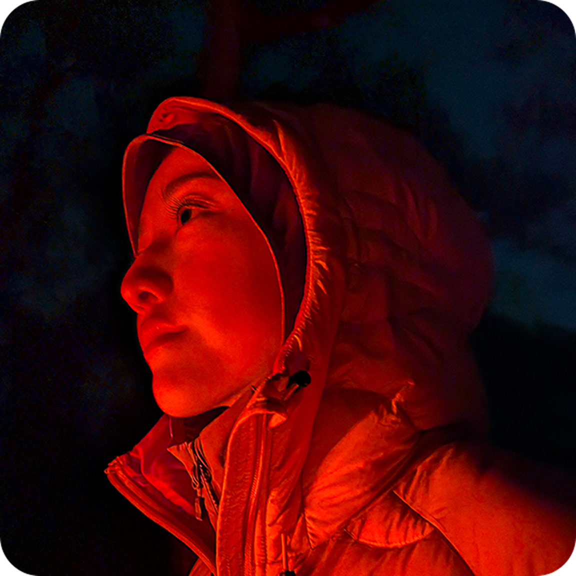 Image of a woman outside in low lighting with red glow.