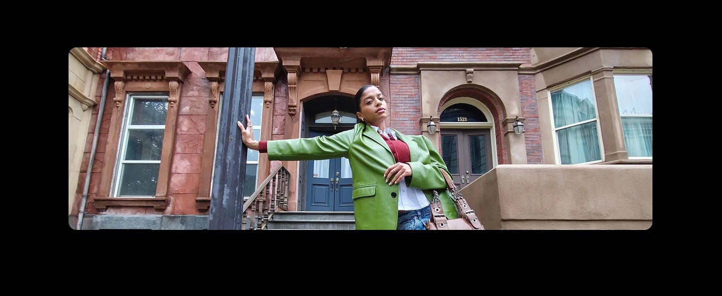 A woman in a green jacket stands confidently against a lamppost in front of brownstone townhouses with a visible address 1521.