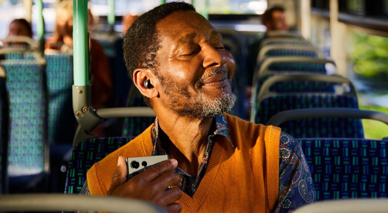 Image of a person on a bus using earbuds to listen to content on their phone
